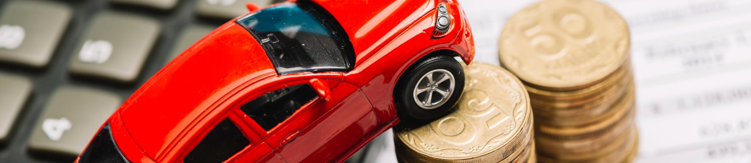 a red model car against a stack of coins and a calculator