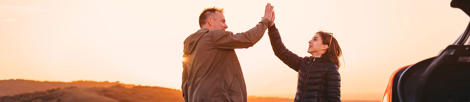 Father and daughter high fiving next to new car