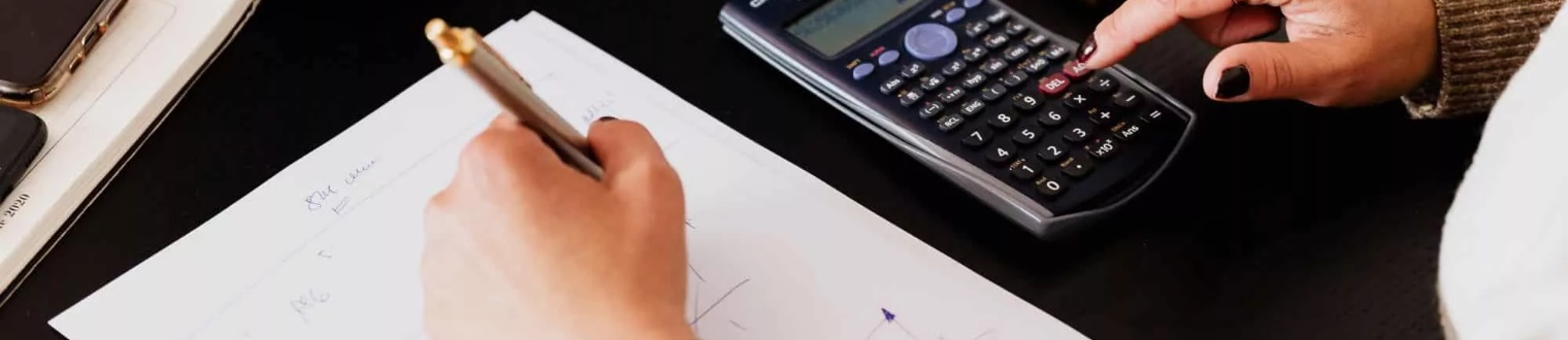 a person writing on a notepad and on their calculator
